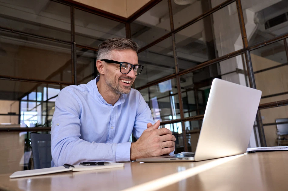 Happy mature business man looking at laptop having virtual meeting in office